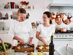 two women in the kitchen preparing food on a cutting board and smiling at each other