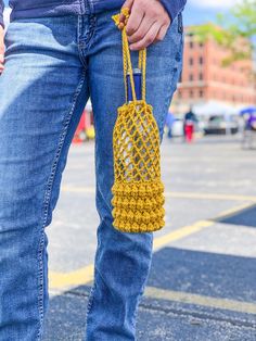 a person wearing blue jeans and holding a yellow crochet purse in their hand