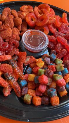 a black plate topped with lots of different colored candies next to a small container