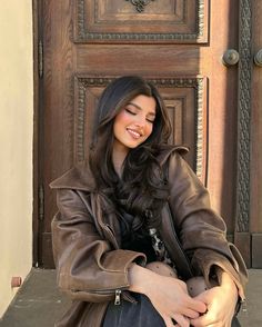 a woman sitting on the ground in front of a wooden door with her hands crossed