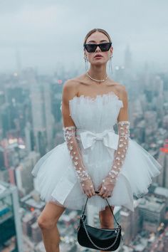 a woman standing on top of a building with her hands in her pockets and wearing gloves