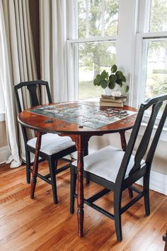 a wooden table with two chairs and a book on it in front of a window