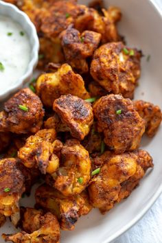 a white plate topped with fried cauliflower next to a bowl of ranch dressing