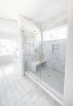 a white bathroom with marble tile flooring and gold accents on the shower door, toilet and bathtub