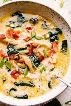 a white bowl filled with chicken, spinach and cheese soup on top of a table