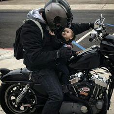 a man on a motorcycle with a baby sitting on the seat and wearing a helmet