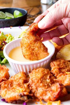 a person dipping something into a small bowl of sauce on top of some fried food