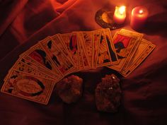 the tarot cards are next to candles and some rocks on a bed with red sheets