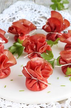 small red flowers are arranged on a white plate with green leaves and sprigs