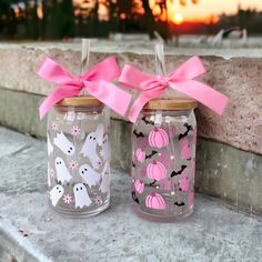 two decorated mason jars with pink bows on the top and ghost decorations on the bottom