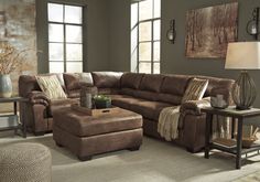 a living room with a sectional couch and footstool in front of two windows