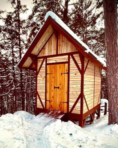 a small wooden outhouse in the middle of snow covered ground with trees around it