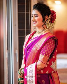 a woman in a red and pink sari smiles at the camera while standing next to a doorway