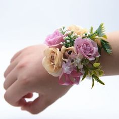 a wrist corsage with flowers and greenery on it's arm, against a white background