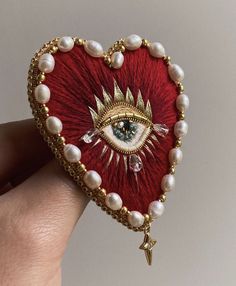 a hand holding a heart shaped brooch with an eye on it's side