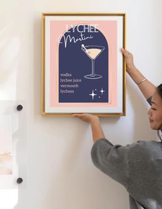 a woman is holding up a framed poster with a martini glass in front of her