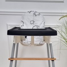 a black and white baby high chair with sheep print on the seat cover, next to a potted plant