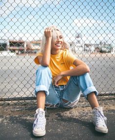 a woman sitting on the ground next to a fence with her hands behind her head