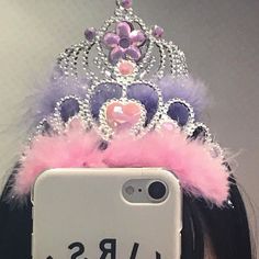 a woman taking a selfie with her phone wearing a tiara and pink feathers