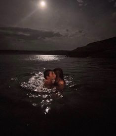 a man and woman kissing in the water at night under a full moon, with dark clouds