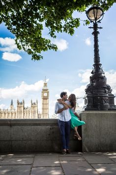 a man and woman standing next to each other near a lamp post with big ben in the background