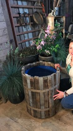 a woman kneeling down next to a wooden barrel filled with water and plants in it