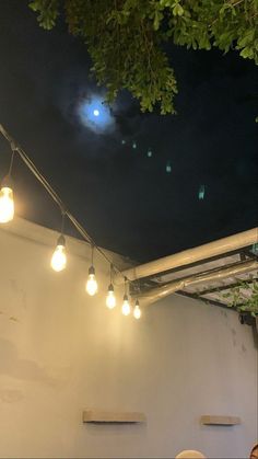 some lights are hanging from the ceiling in an outdoor area with white walls and green trees