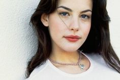 a woman with long dark hair wearing a white t - shirt and a necklace on her neck