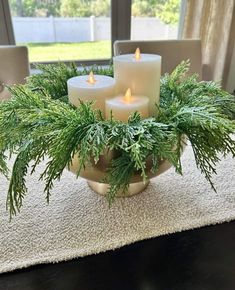 three lit candles sitting on top of a bowl filled with pine needles and greenery