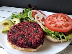 a white plate topped with a beet and lettuce sandwich next to sliced tomatoes