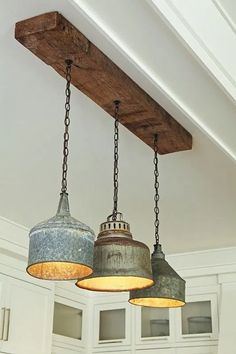 three light fixtures hanging from a wooden beam in a kitchen with white cabinets and cupboards