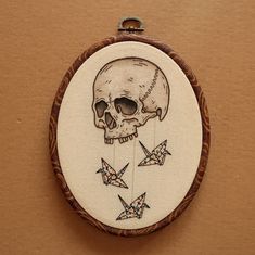 an embroidered skull and origami cranes on a wooden frame hanging from a wall