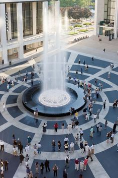 a group of people standing around a fountain in the middle of a courtyard with columns