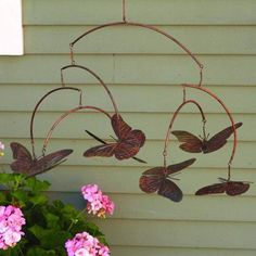 a wind chime hanging from the side of a house with pink flowers in front of it