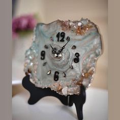 a clock made out of glass sitting on top of a white table next to a pink flower