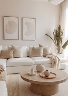 a living room filled with white furniture and paintings on the wall above it's coffee table