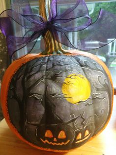 a decorated pumpkin sitting on top of a wooden table in front of a window with purple ribbon