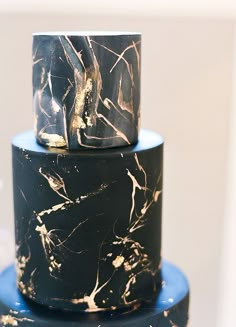 a three tiered black and gold marbled cake with blue icing on top