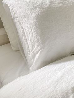 a white bed with two pillows and one pillow on top of the headboard in front of it