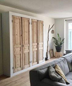 a living room filled with furniture next to a large window and wooden doors on the wall