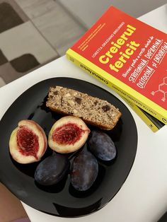 a black plate topped with figs next to a book on top of a table