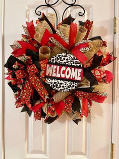 a red and black welcome wreath hanging on a white door with the word welcome written on it