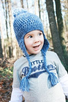 a young boy wearing a blue knitted hat and scarf in the woods with trees behind him