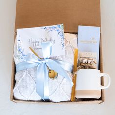 a gift box with coffee mug, tea towel and other items in it for someone's birthday