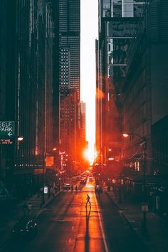 a person walking down the middle of a city street at sunset with buildings in the background