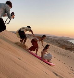 three people standing on top of a pink surfboard while another person films them in the background