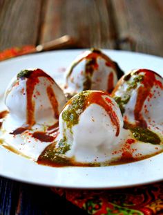 three scoops of ice cream covered in sauce on a white plate with red and green decorations