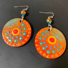 two orange and blue earrings with circles on them sitting on a black surface next to each other