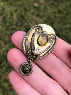 Here is an early Victorian brooch with a genuine citrine stone set into the middle (tested on a Presidium Gem Tester). This stone also looks like it might have a foil back as there is some black speckling visible (a sign the foil has eroded over time). The stone has a crimped setting, a sign of an earlier 19th century piece. There is a dangle with a small pearl in it. The metal is gold filled. The back: I have not been able to remove the glass. It has a later picture in there that looks to be fr Collectible Gold Brooches With Gemstones, Antique Oval Gemstone Brooches, Antique Gold Brooch With Gemstone, Antique Oval Gemstone Brooch, Antique Gold Gemstone Brooch, Victorian Gold Locket Brooches, Victorian Gold Brooch With Locket, Ornate Gold Locket Brooches, Antique Yellow Gold Brooches With Gemstone