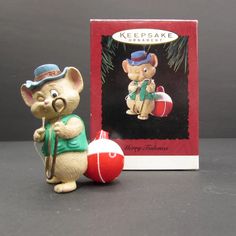 a mouse figurine next to a christmas ornament in front of a box